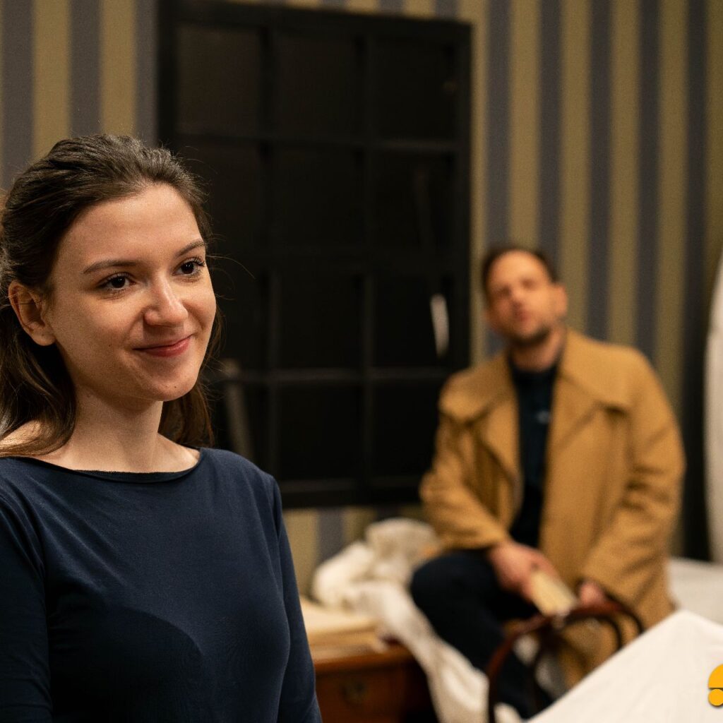 Egy nő mosolyog a képen, a háttérben elmosódva egy férfi a nőre mosolyog