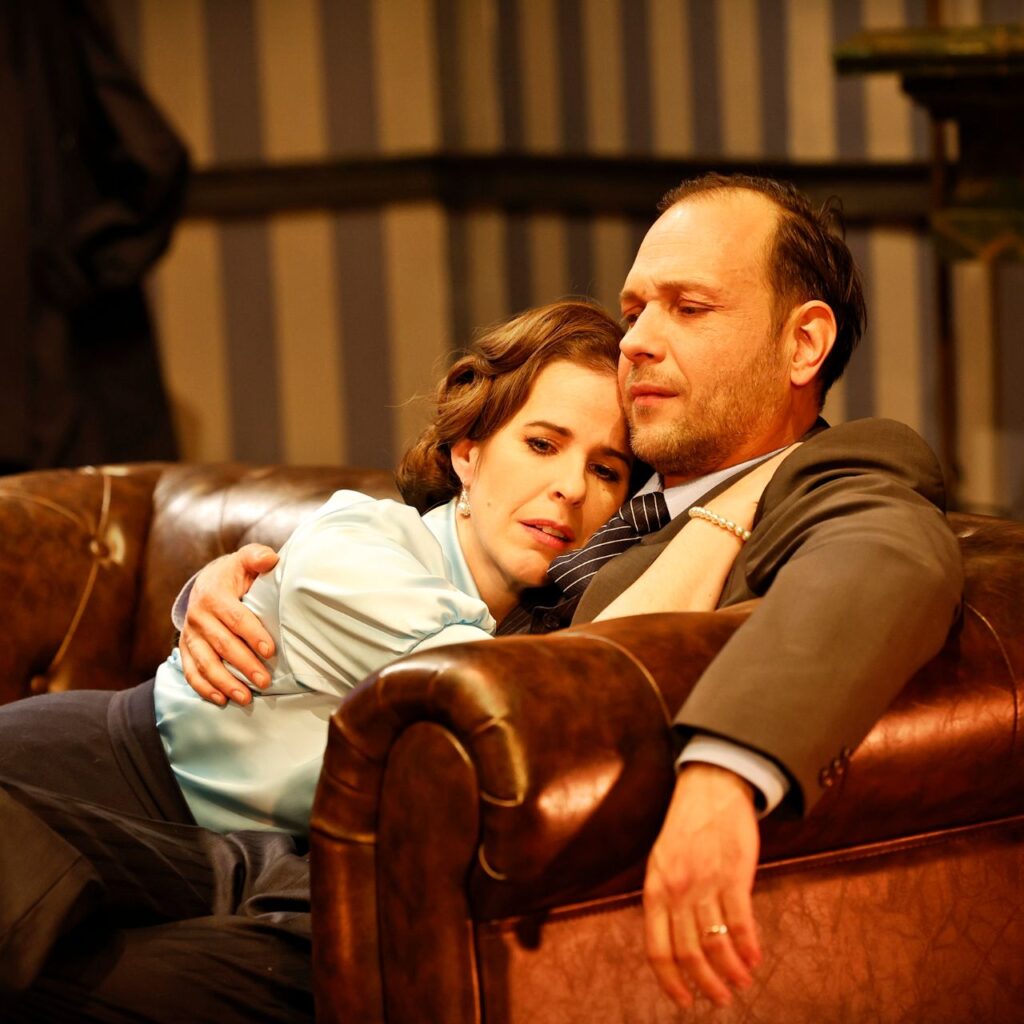 Egy nő és egy férfi ül egy barna bőr kanapén, a férfi átkarolja a nőt, és mind a ketten szomorúan néznek