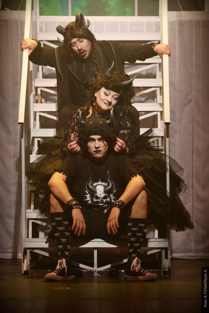 Három ördögnek öltözött ember ül egymás mögött egy fehér lépcsőn és énekelnek