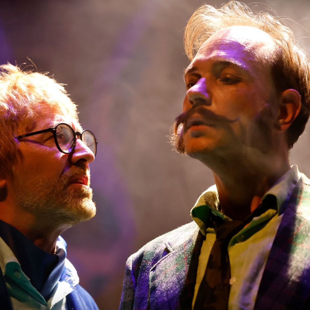 A Kék róka című színházi előadás két férfi szereplője feszültséggel teli párbeszéd közben a színpadon, drámai fényekben.