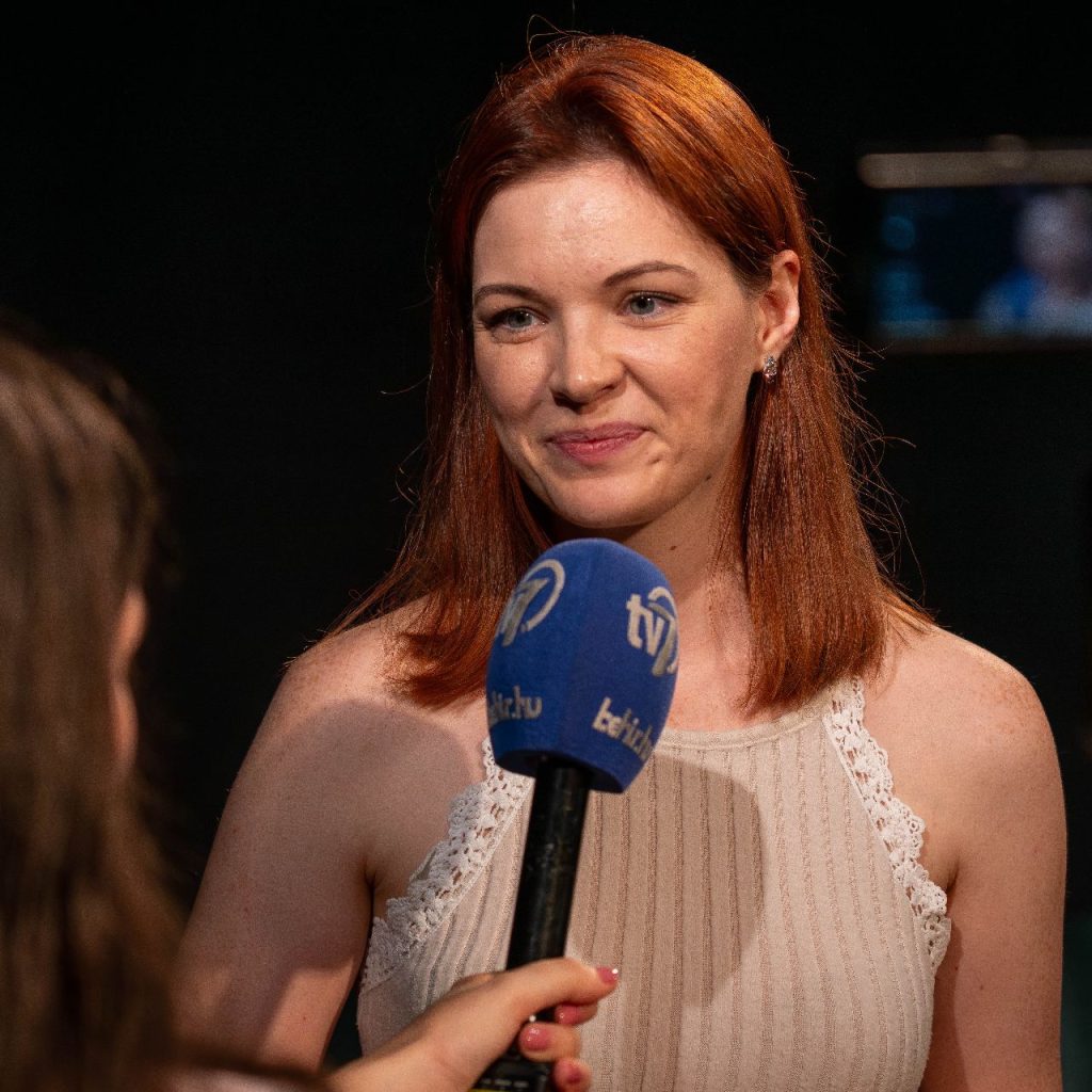 A Kék róka című előadás olvasópróbáján egy nő interjút ad a TV7 csatornának, miközben egy mikrofont tartanak elé.