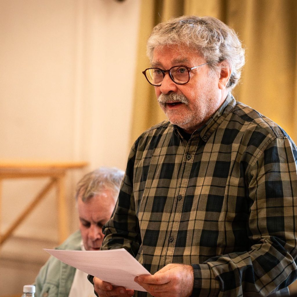 A Látni a láthatatlant című előadás olvasópróbáján egy szereplő felolvas a társulat előtt.