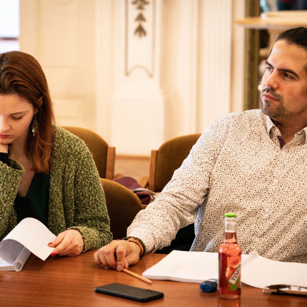 A Látni a láthatatlant című előadás olvasópróbáján két szereplő ül egymás mellett, előttük szövegkönyv és jegyzetek az asztalon.