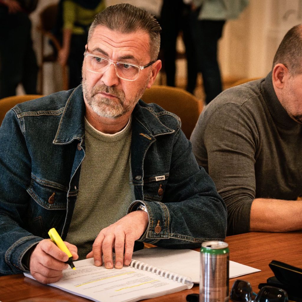 A Látni a láthatatlant című előadás olvasópróbáján két férfi jegyzetel az asztalnál, előttük a darab szövegkönyve.