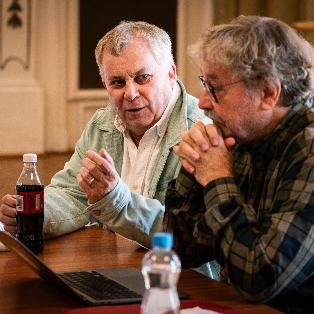 A Látni a láthatatlant című előadás olvasópróbáján két alkotó beszélget az asztalnál, előttük laptop és jegyzetek.