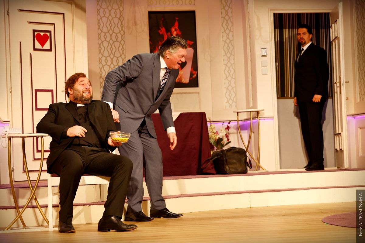 A színművészek a Legénybúcsú című előadásban jelenet közben a színpadon jóízűen nevetnek, a harmadik színművész meglepetten figyeli őket.