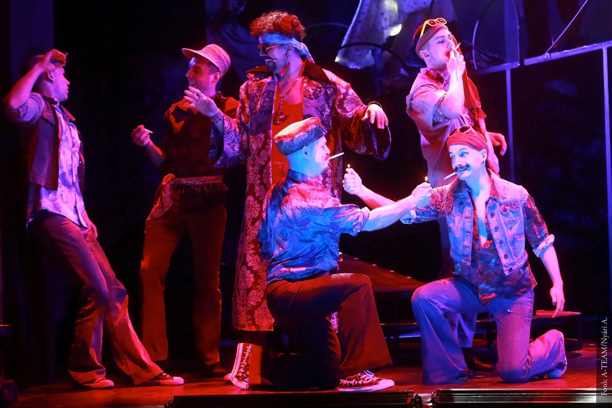 A színművészek a Balkán Kobra című előadás egyik jelenetében a színpadon táncolnak, dohányoznak.