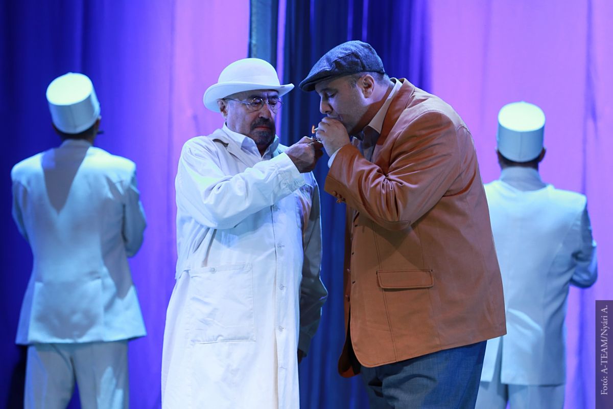 A színművészek a Liliom című előadásban jelenet közben a színpadon, miközben cigarettát nyújt az egyik a másiknak.