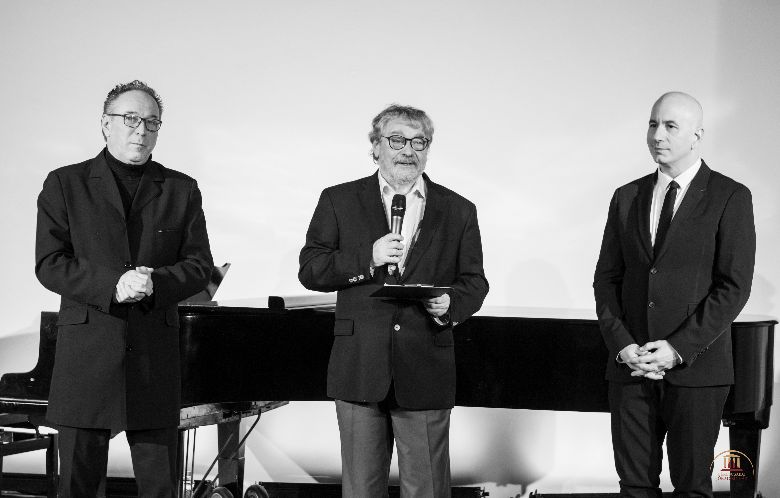 Három férfi áll egy zongora előtt, bal oldalon Fekete Péter látható, középen Seregi Zoltán, jobbról pedig Herczeg T. Tamás