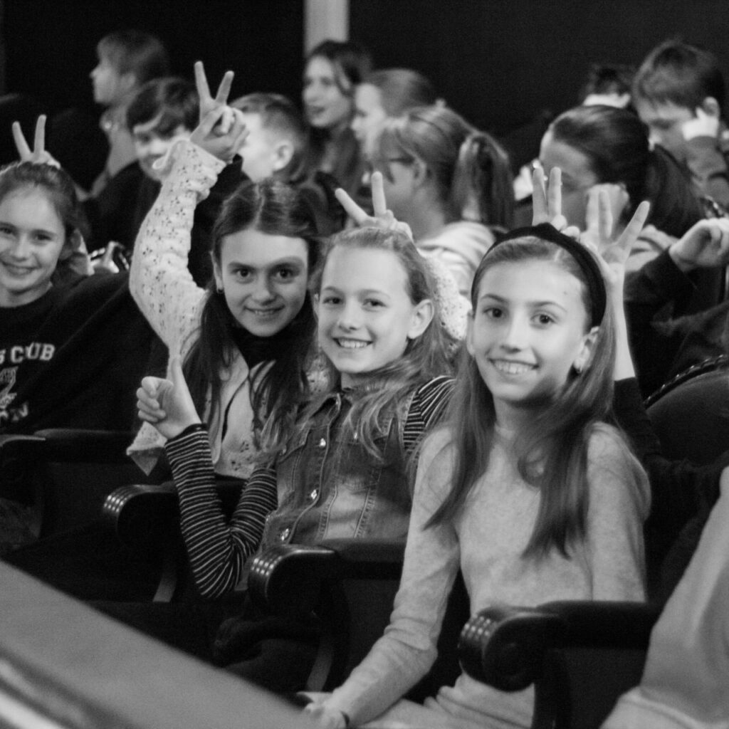 fekete-fehér képen gyerekek ülnek több sorban és mosolyognak a kamerába, kezeikkel nyuszi fület mutatnak egymás fején