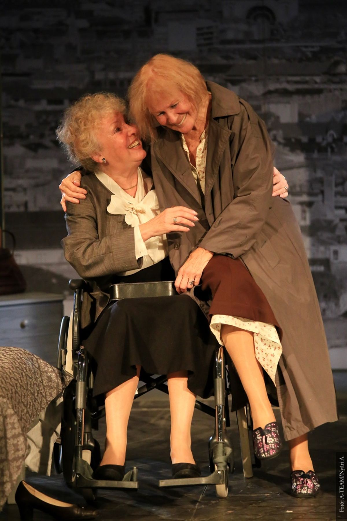 A színművészek a Macskajáték című előadásban jelenet közben vidáman ülnek, egymást átkarolva a színpadon.