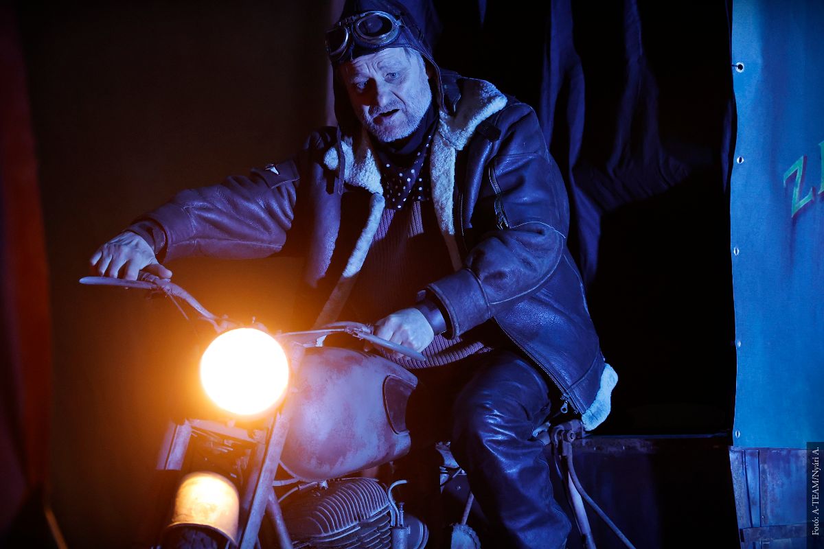 A színművész az Országúton című darabban jelenet közben motoron ülve.